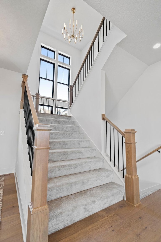 stairs with a chandelier, a textured ceiling, hardwood / wood-style flooring, and vaulted ceiling