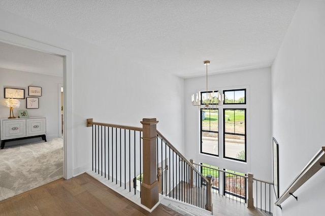 staircase with hardwood / wood-style floors, a textured ceiling, and an inviting chandelier