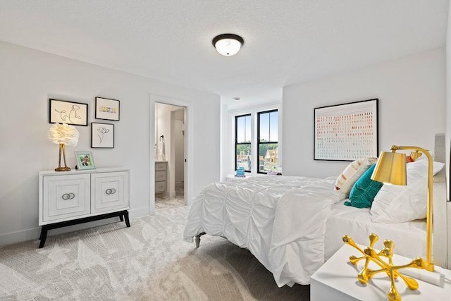 bedroom featuring ensuite bathroom, light colored carpet, and a textured ceiling