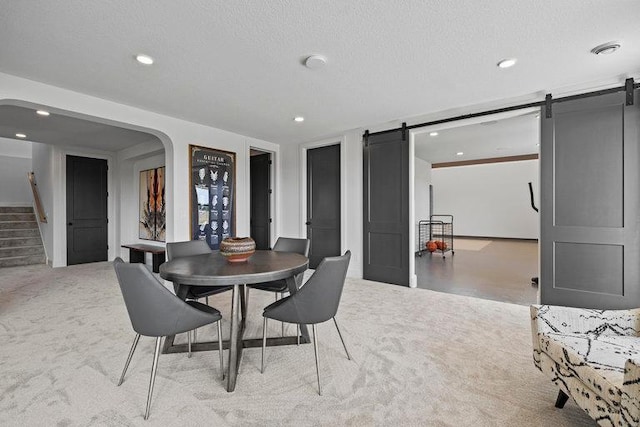 dining space featuring a barn door, light carpet, and a textured ceiling