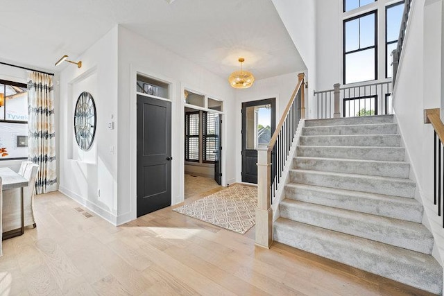 foyer with light wood-type flooring, visible vents, baseboards, and stairs