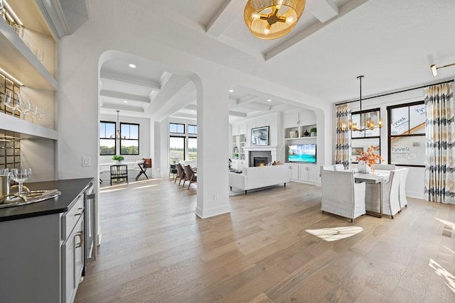 interior space with light wood-style floors, a warm lit fireplace, beam ceiling, and an inviting chandelier