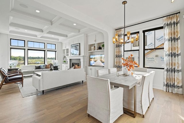 dining space featuring light wood finished floors, a warm lit fireplace, built in features, coffered ceiling, and beam ceiling