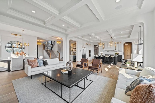 living area with arched walkways, light wood finished floors, stairway, and a notable chandelier