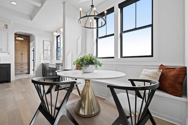 dining area with light wood finished floors, arched walkways, coffered ceiling, an inviting chandelier, and a decorative wall