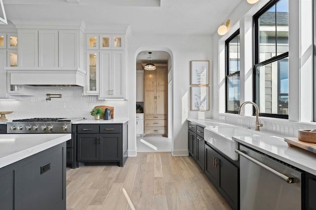 kitchen featuring arched walkways, a sink, white cabinets, light countertops, and dishwasher