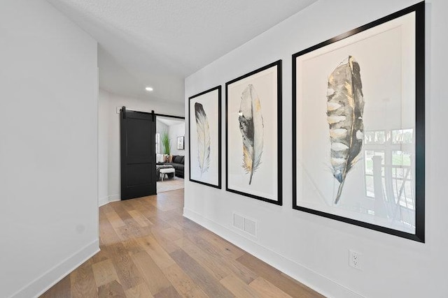 hall featuring baseboards, visible vents, light wood finished floors, and a barn door