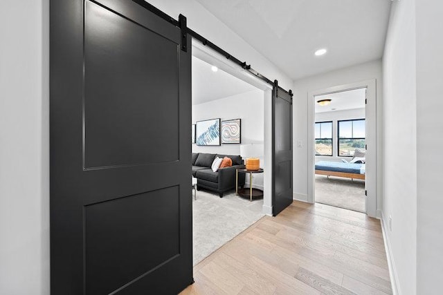 corridor with a barn door, light wood-type flooring, light colored carpet, and baseboards