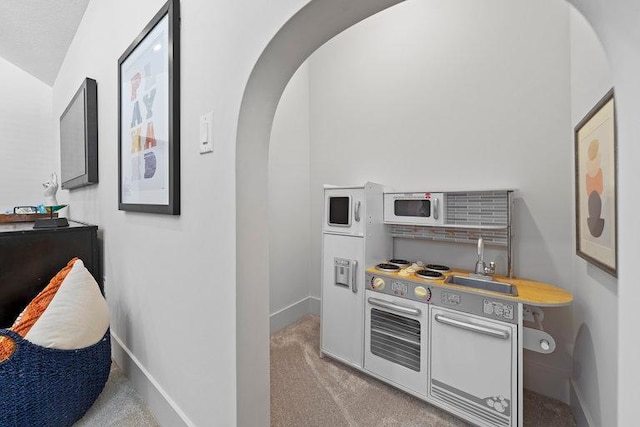 interior space featuring carpet floors, white microwave, baseboards, and arched walkways