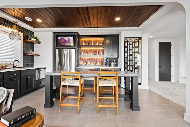 bar featuring arched walkways, a sink, wood ceiling, freestanding refrigerator, and tasteful backsplash