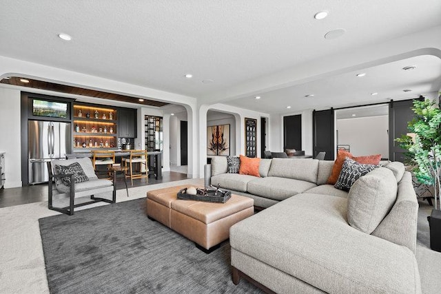 living area with a barn door, arched walkways, bar, a textured ceiling, and recessed lighting