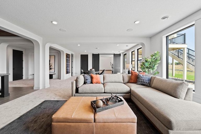 carpeted living room with arched walkways, a textured ceiling, and recessed lighting