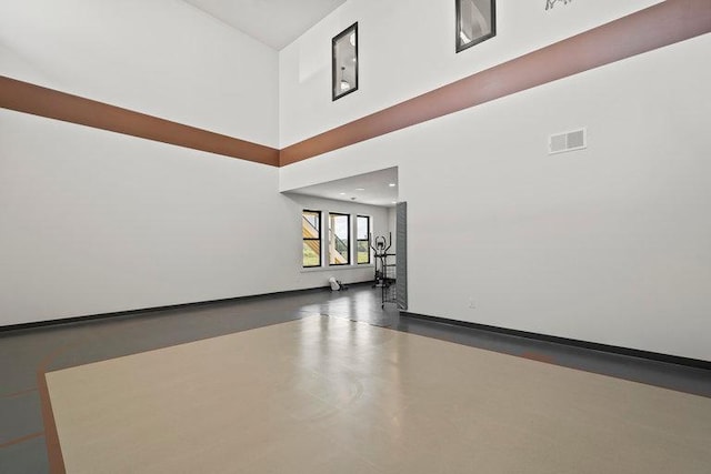 unfurnished living room featuring a high ceiling, concrete floors, visible vents, and baseboards