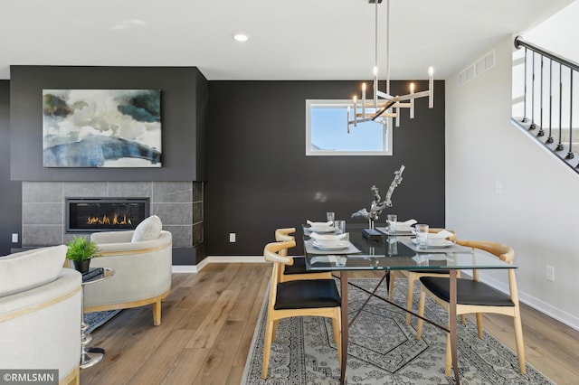 dining area featuring hardwood / wood-style flooring, a tiled fireplace, and an inviting chandelier