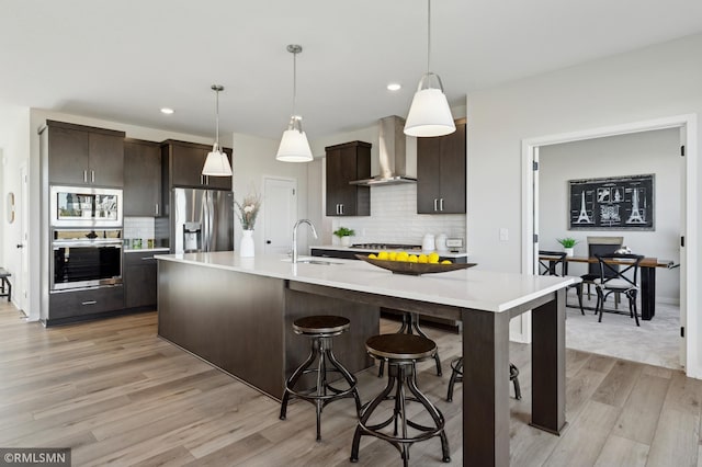 kitchen featuring sink, appliances with stainless steel finishes, wall chimney range hood, and dark brown cabinets