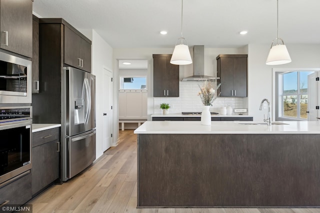 kitchen with appliances with stainless steel finishes, dark brown cabinets, wall chimney exhaust hood, and pendant lighting