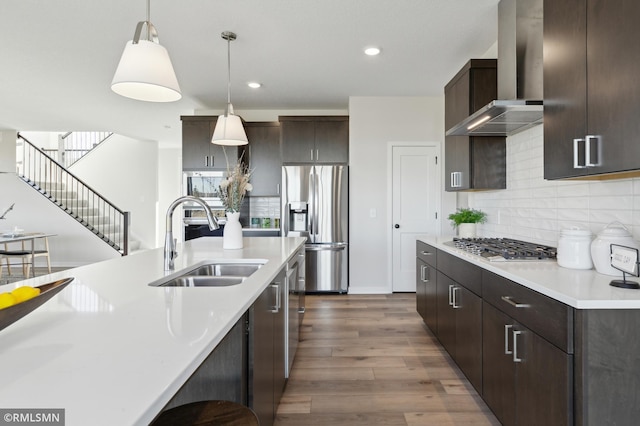 kitchen with stainless steel appliances, wall chimney range hood, pendant lighting, dark brown cabinetry, and sink