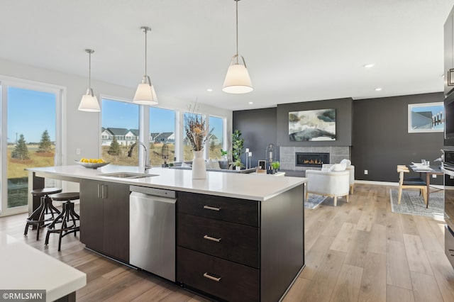 kitchen with dishwasher, an island with sink, sink, hanging light fixtures, and a tiled fireplace