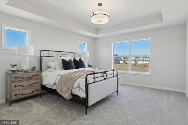 bedroom with light carpet and a tray ceiling