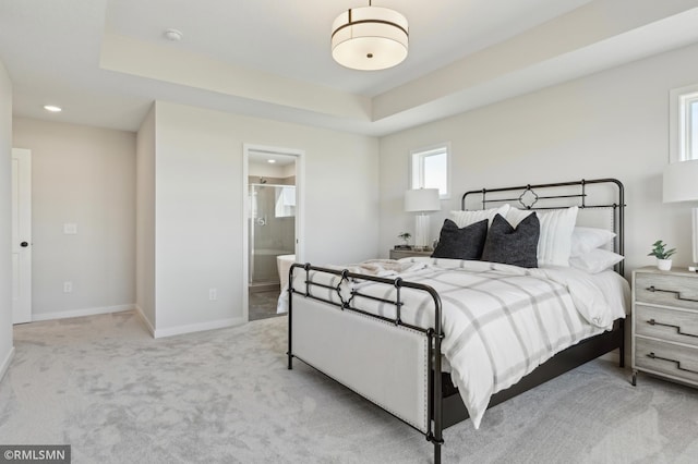 carpeted bedroom featuring a raised ceiling and ensuite bath