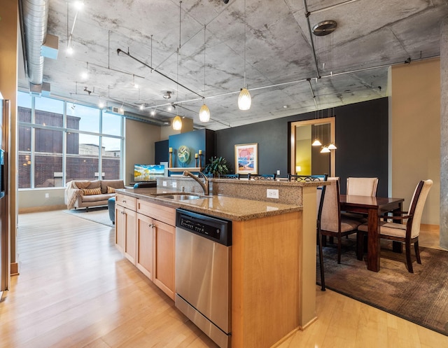 kitchen with dishwasher, sink, dark stone countertops, pendant lighting, and light hardwood / wood-style floors