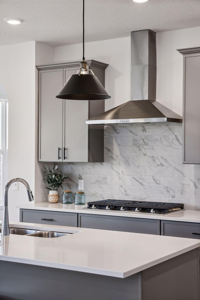 kitchen with pendant lighting, gray cabinets, wall chimney exhaust hood, and sink