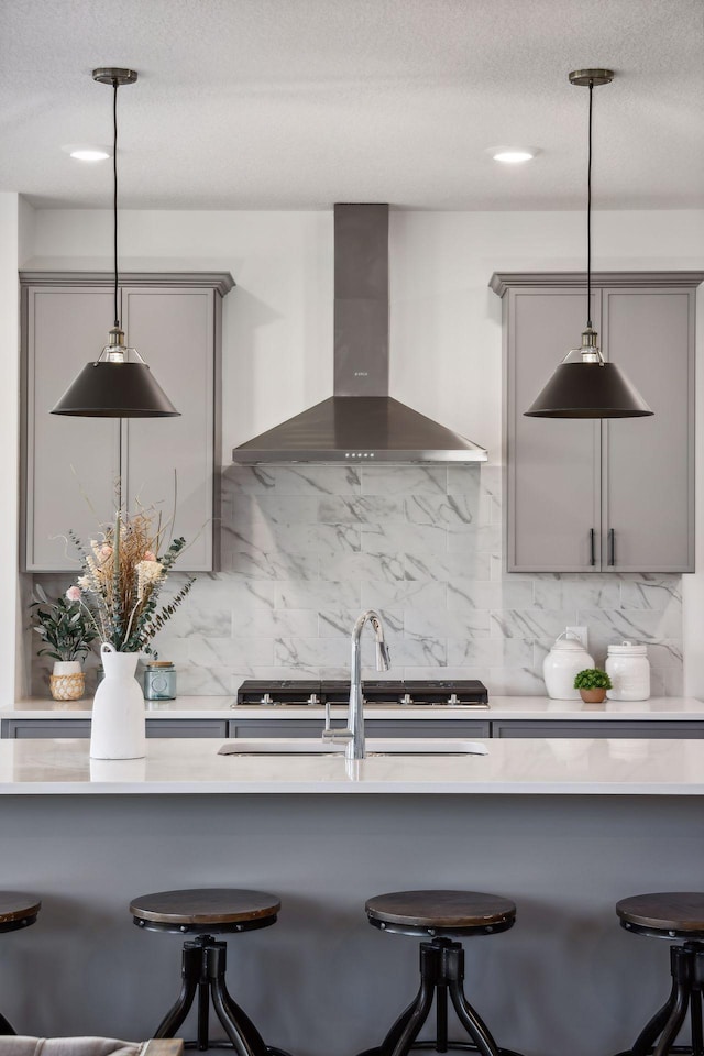 kitchen featuring tasteful backsplash, gray cabinets, hanging light fixtures, and wall chimney range hood