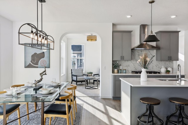 kitchen with pendant lighting, wall chimney range hood, sink, gray cabinets, and stainless steel gas cooktop