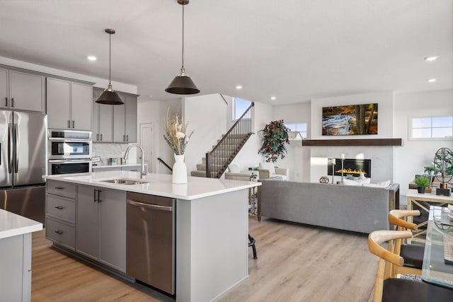 kitchen featuring appliances with stainless steel finishes, sink, a center island with sink, gray cabinets, and hanging light fixtures