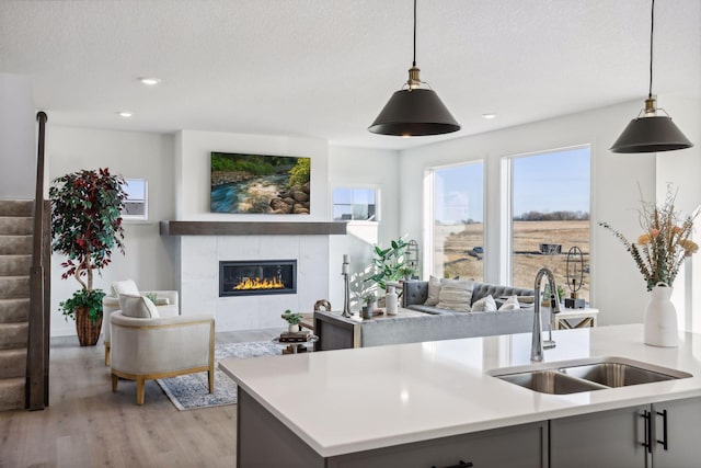 kitchen featuring a tile fireplace, sink, a textured ceiling, decorative light fixtures, and light wood-type flooring