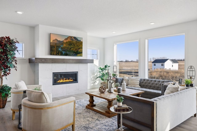 living room with a textured ceiling, hardwood / wood-style flooring, a healthy amount of sunlight, and a tiled fireplace