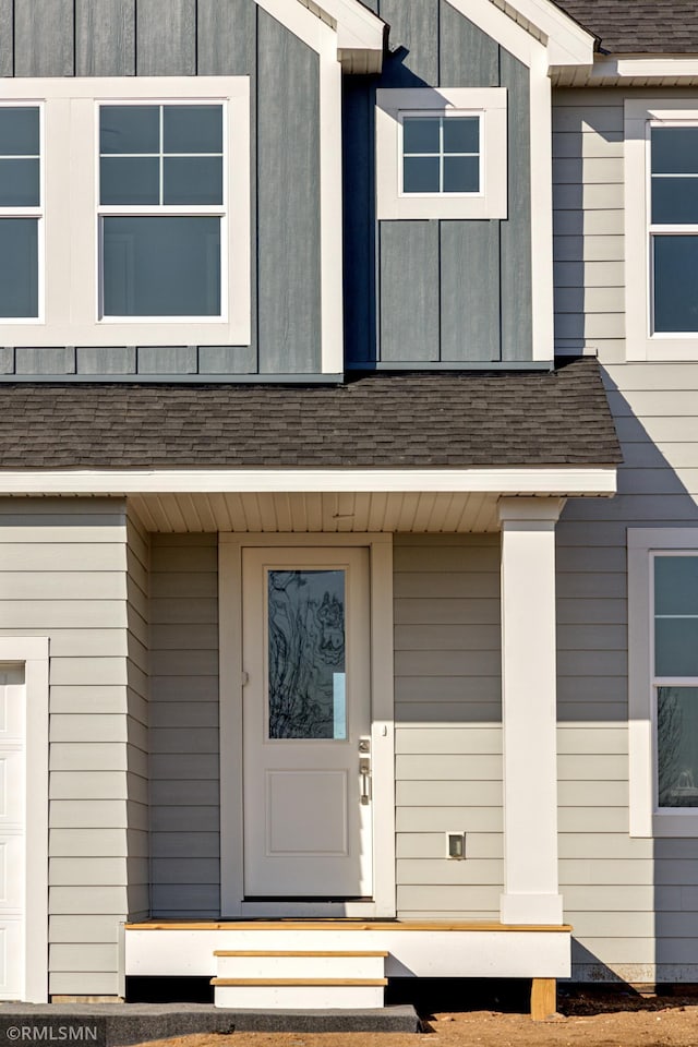 doorway to property featuring a garage and roof with shingles