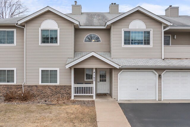 multi unit property with driveway, covered porch, a chimney, a garage, and brick siding