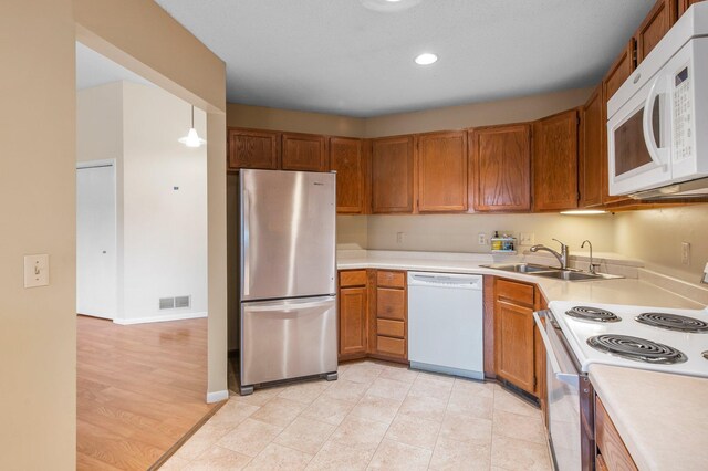 kitchen with visible vents, brown cabinets, a sink, white appliances, and light countertops