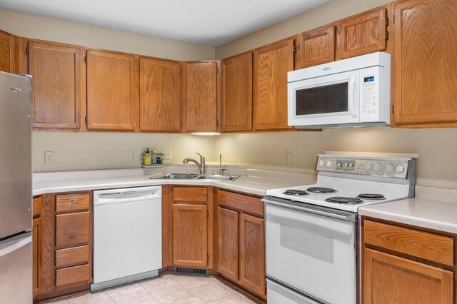kitchen featuring brown cabinets, white appliances, light countertops, and a sink