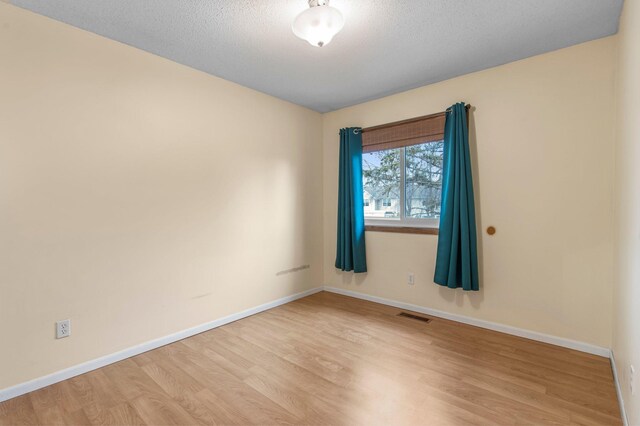 spare room featuring light wood-type flooring, visible vents, baseboards, and a textured ceiling