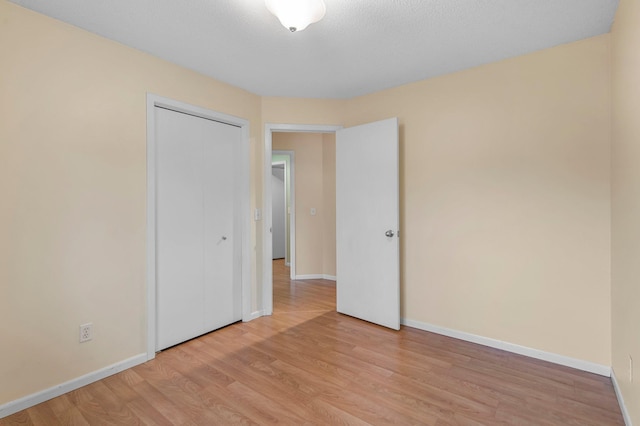 unfurnished bedroom featuring baseboards, light wood-type flooring, and a closet