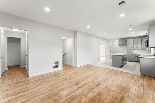 kitchen featuring light wood-type flooring, gray cabinets, a kitchen island, and sink