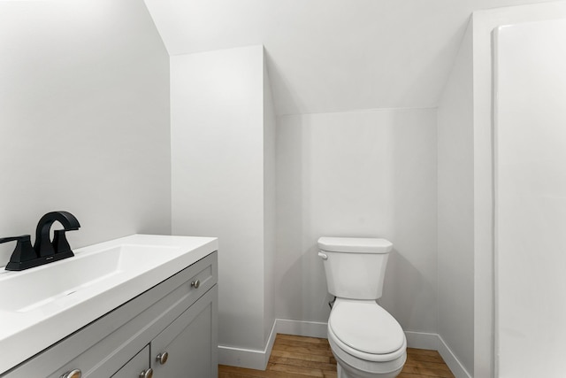 bathroom featuring vanity, wood-type flooring, lofted ceiling, and toilet