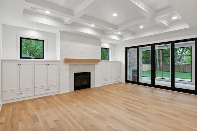 unfurnished living room featuring beam ceiling, a tiled fireplace, light hardwood / wood-style flooring, and a healthy amount of sunlight