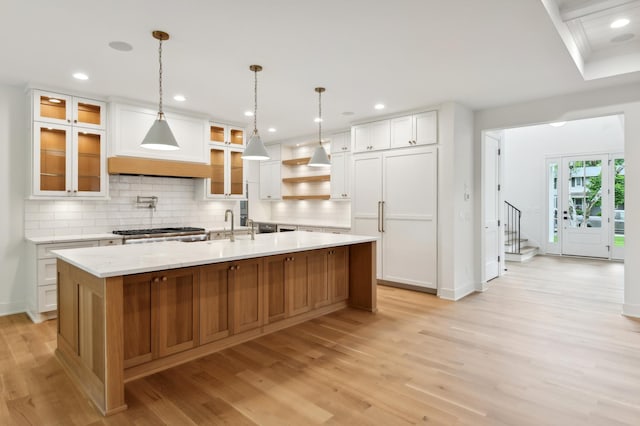 kitchen with premium range hood, a large island with sink, decorative backsplash, light hardwood / wood-style floors, and white cabinetry