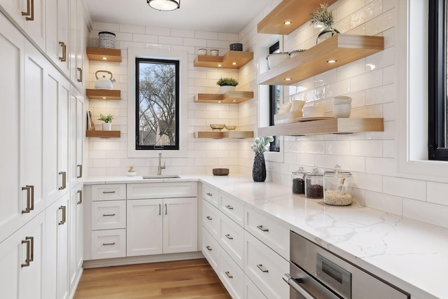 kitchen featuring light stone countertops, sink, tasteful backsplash, light hardwood / wood-style floors, and white cabinets