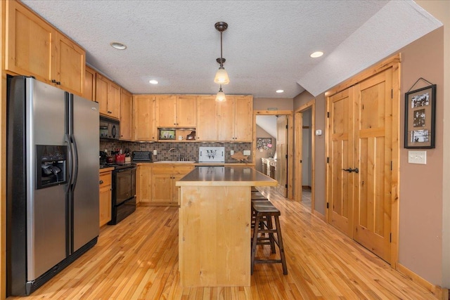 kitchen with a breakfast bar, a sink, black appliances, and light wood-type flooring