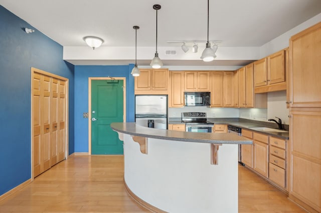 kitchen with a kitchen bar, appliances with stainless steel finishes, sink, decorative light fixtures, and light hardwood / wood-style floors