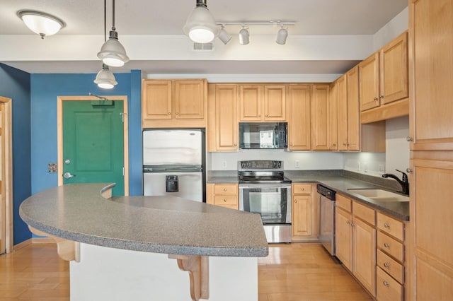 kitchen featuring light wood-type flooring, stainless steel appliances, sink, light brown cabinets, and decorative light fixtures