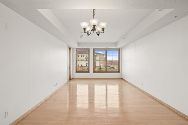 spare room with a tray ceiling, a chandelier, and light wood-type flooring