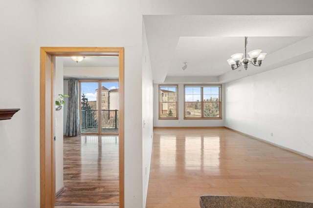 unfurnished living room with light hardwood / wood-style flooring, a wealth of natural light, and a chandelier