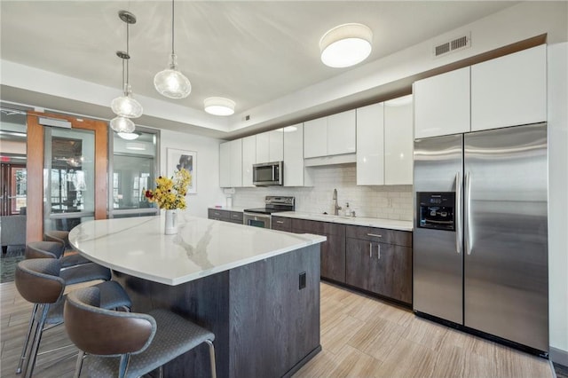 kitchen with a center island, sink, stainless steel appliances, pendant lighting, and white cabinets