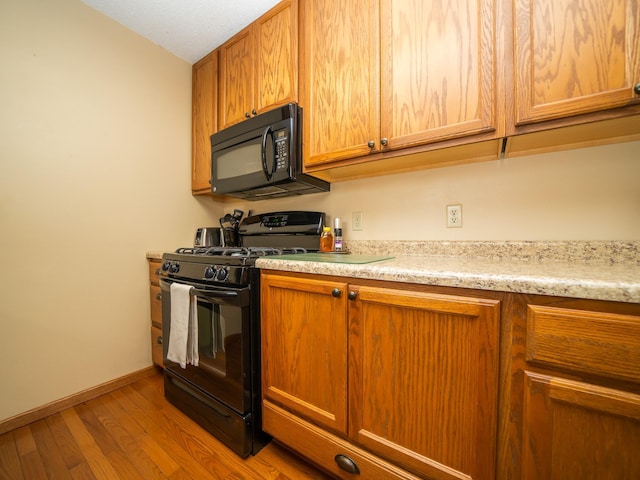 kitchen with light hardwood / wood-style floors, light stone counters, and black appliances