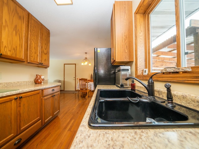 kitchen featuring hardwood / wood-style flooring, black refrigerator, a notable chandelier, pendant lighting, and sink